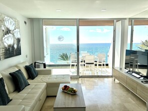 Una sala de estar moderna con un sofá, una mesa de centro con fruta y un balcón con vistas al mar.