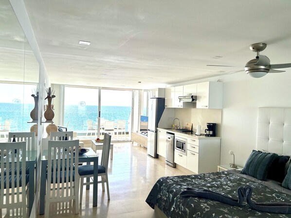 Una habitación de hotel moderna con balcón, zona de comedor, kitchenette y cama.