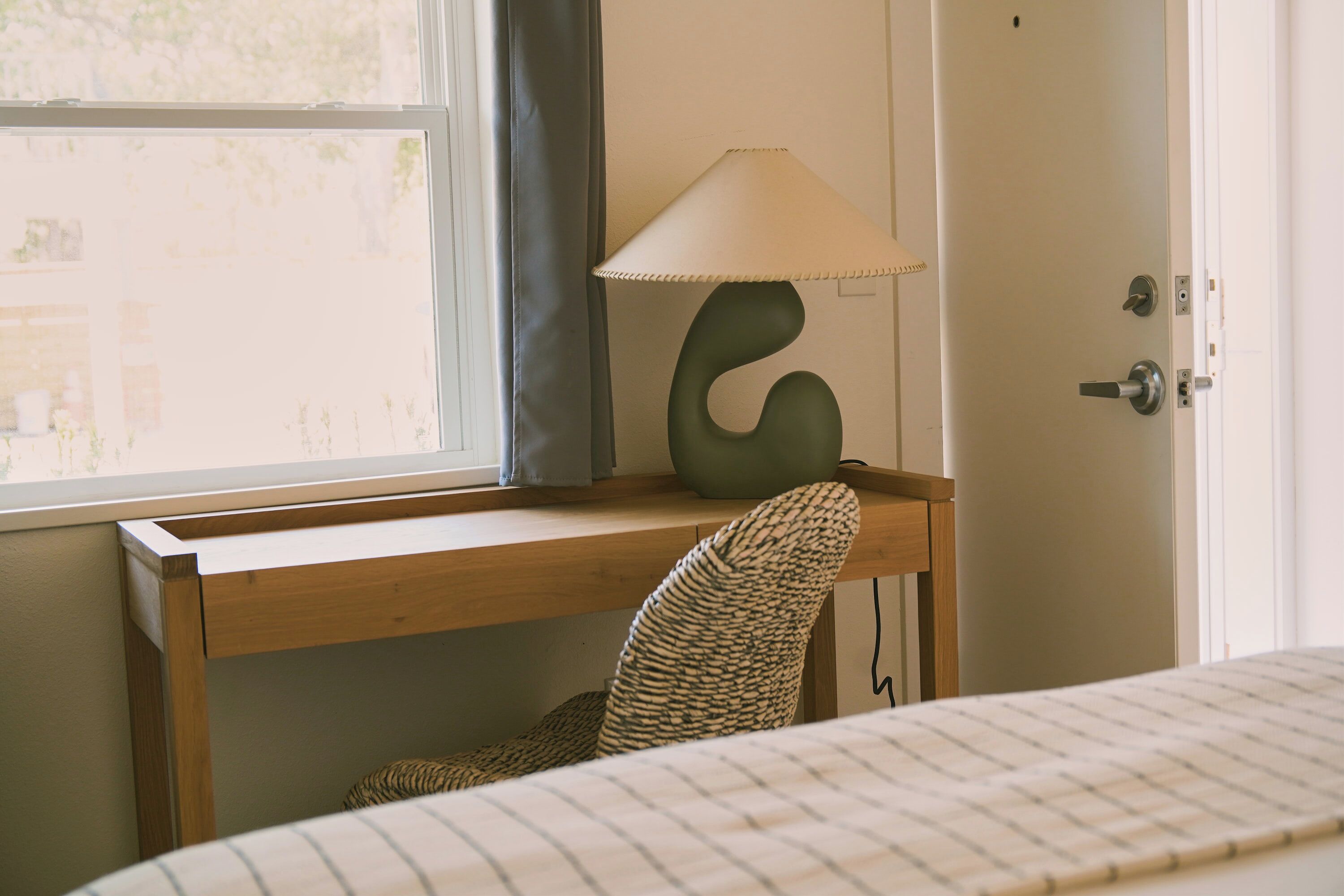 A room with a wooden desk, a lamp, a chair, and a bed.