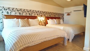 A hotel room with two beds, a floral wallpaper, a ceiling light, and a wall-mounted air conditioner.