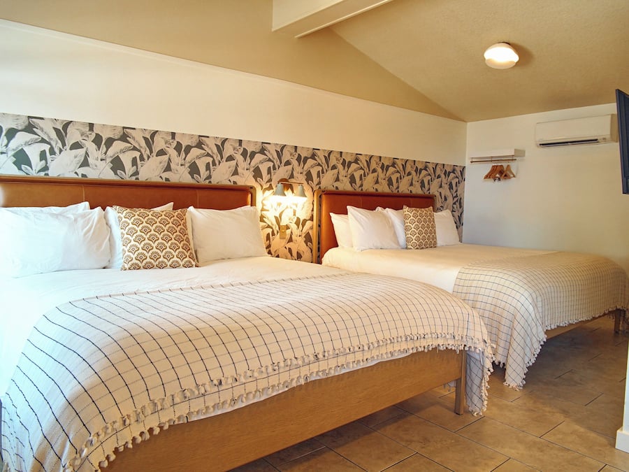 A hotel room with two beds, a floral wallpaper, a ceiling light, and a wall-mounted air conditioner.