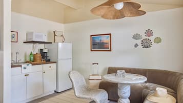 Ett kompakt bostadsutrymme med ett litet kök, en flätad stol, ett runt bord och en soffa.