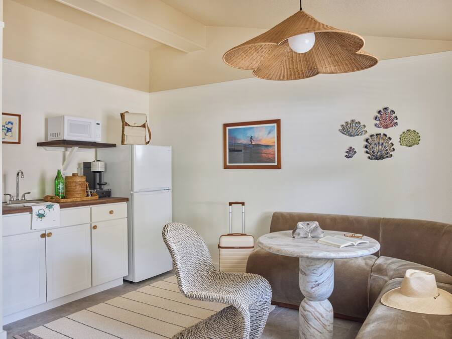 Ett kompakt bostadsutrymme med ett litet kök, en flätad stol, ett runt bord och en soffa.