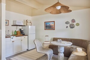 Un espacio habitable compacto con kitchenette, una silla tejida, una mesa redonda y un sofá.