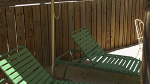 A wooden fence with a blue and white striped umbrella, two green lounge chairs, and a white chair. - Hotel Palms (Atlantic Beach)