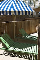 Una valla de madera con un paraguas a rayas azul y blanco, dos sillones verdes y una silla blanca.
