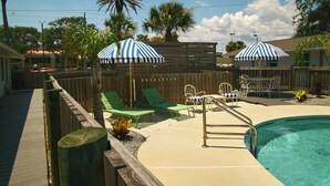 A backyard with a swimming pool, wooden deck, and outdoor furniture.