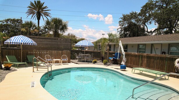 A swimming pool with a wooden deck, lounge chairs, and umbrellas.