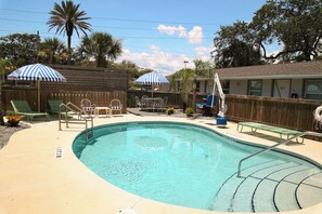 A swimming pool with a wooden deck, lounge chairs, and umbrellas.