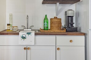 A kitchen with a sink, a coffee maker, a bottle of Mountain Valley Spring Water, and a jar of cream cheese stuffed olives.