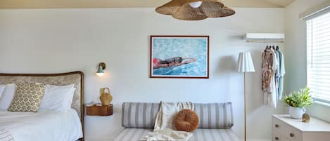A bedroom with a bed, a bedside table with a lamp, a sofa, a coffee table with a book, and a painting on the wall.