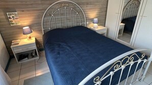 A bedroom with a metal bed frame, a wooden headboard, a bedside table with a lamp, a nightstand, a mirror, and a tiled floor. - Ref 541 - Quiet house close to the beaches and the city center (SOULAC SUR MER)