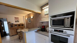 A compact kitchen with a microwave, oven, and a coffee maker. There is a wooden cabinet and a dining area with chairs. - Ref 541 - Quiet house close to the beaches and the city center (SOULAC SUR MER)