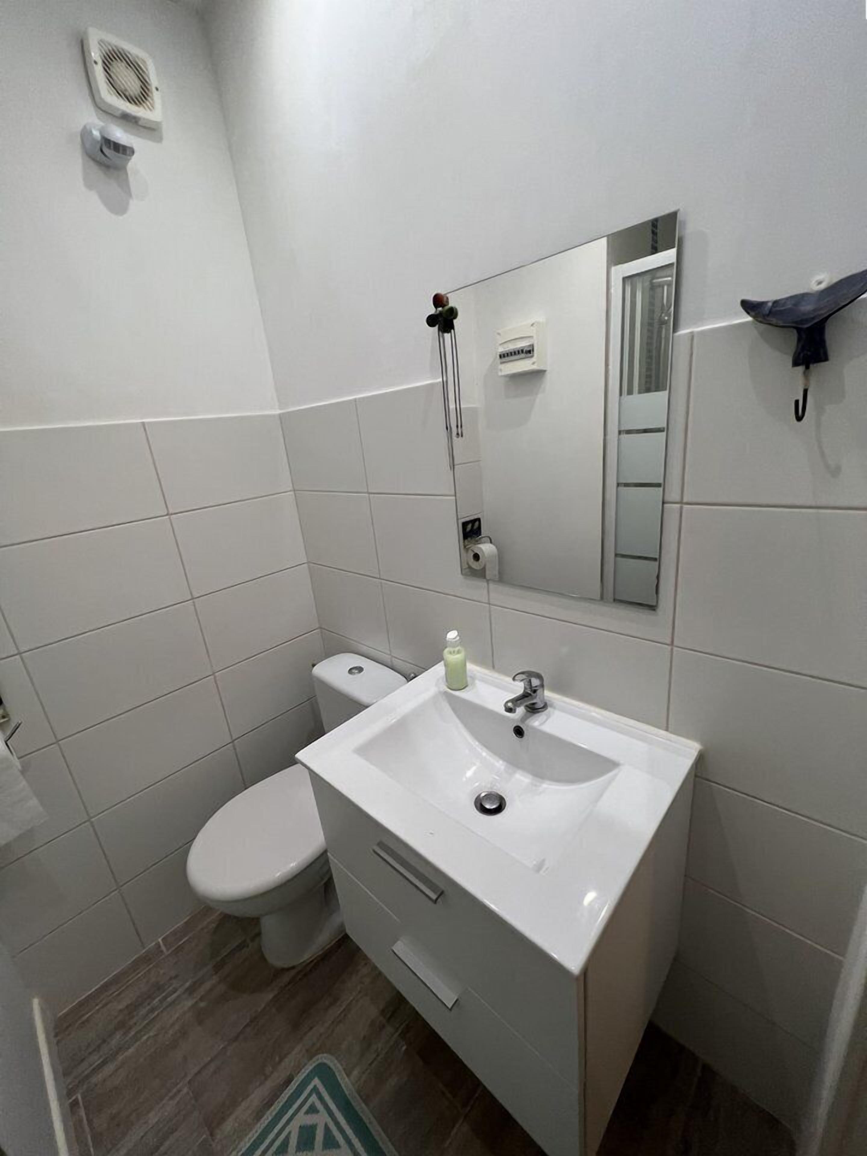 Un baño con lavamanos, espejo y retrete blanco.