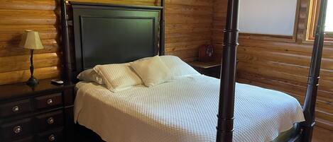 A four-poster bed with a dark headboard, a bedside table with a lamp, and a wooden wall with a clock.