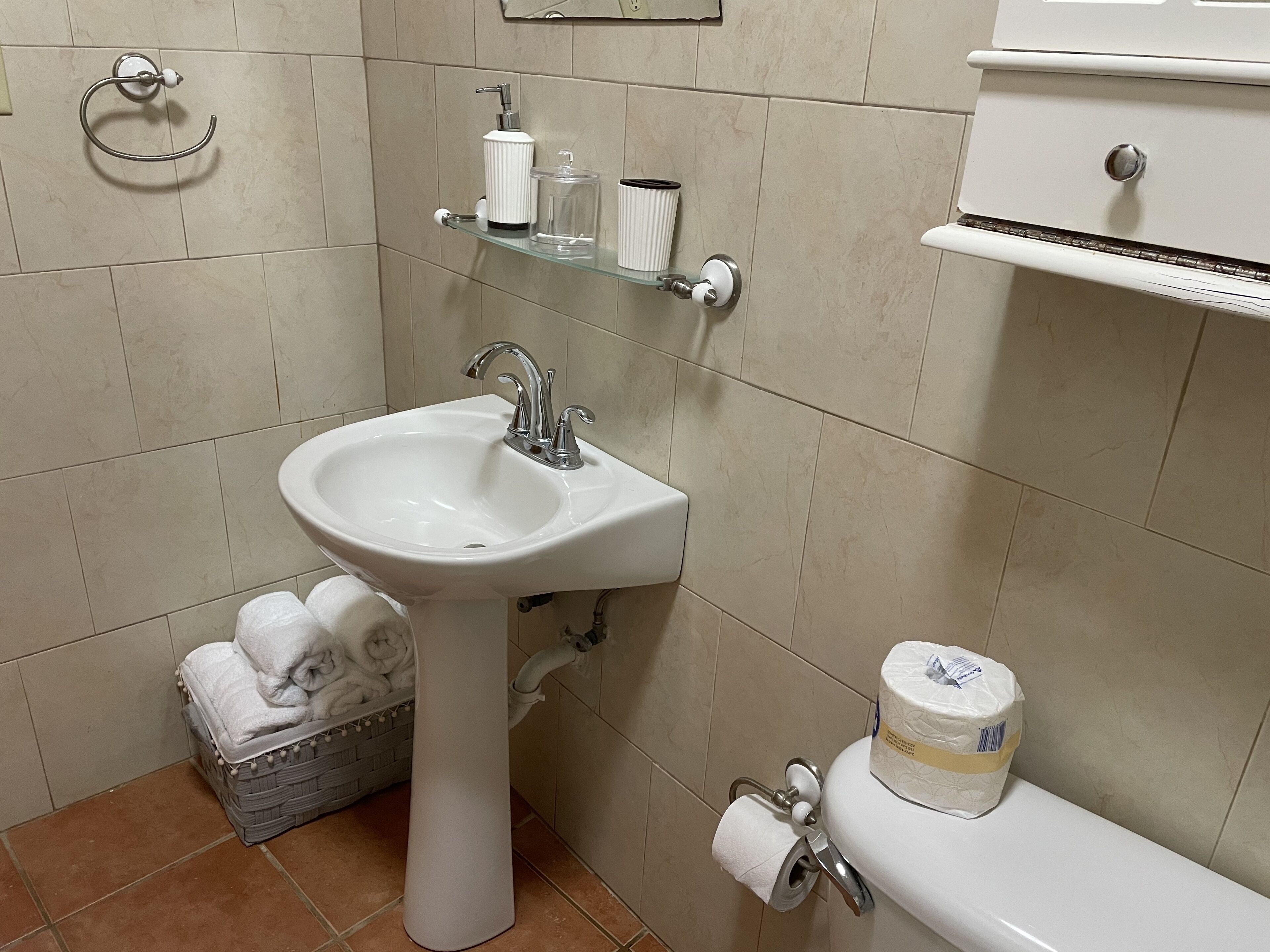 Une salle de bain avec un lavabo blanc, des toilettes, un porte-serviettes et une étagère contenant des articles de toilette.