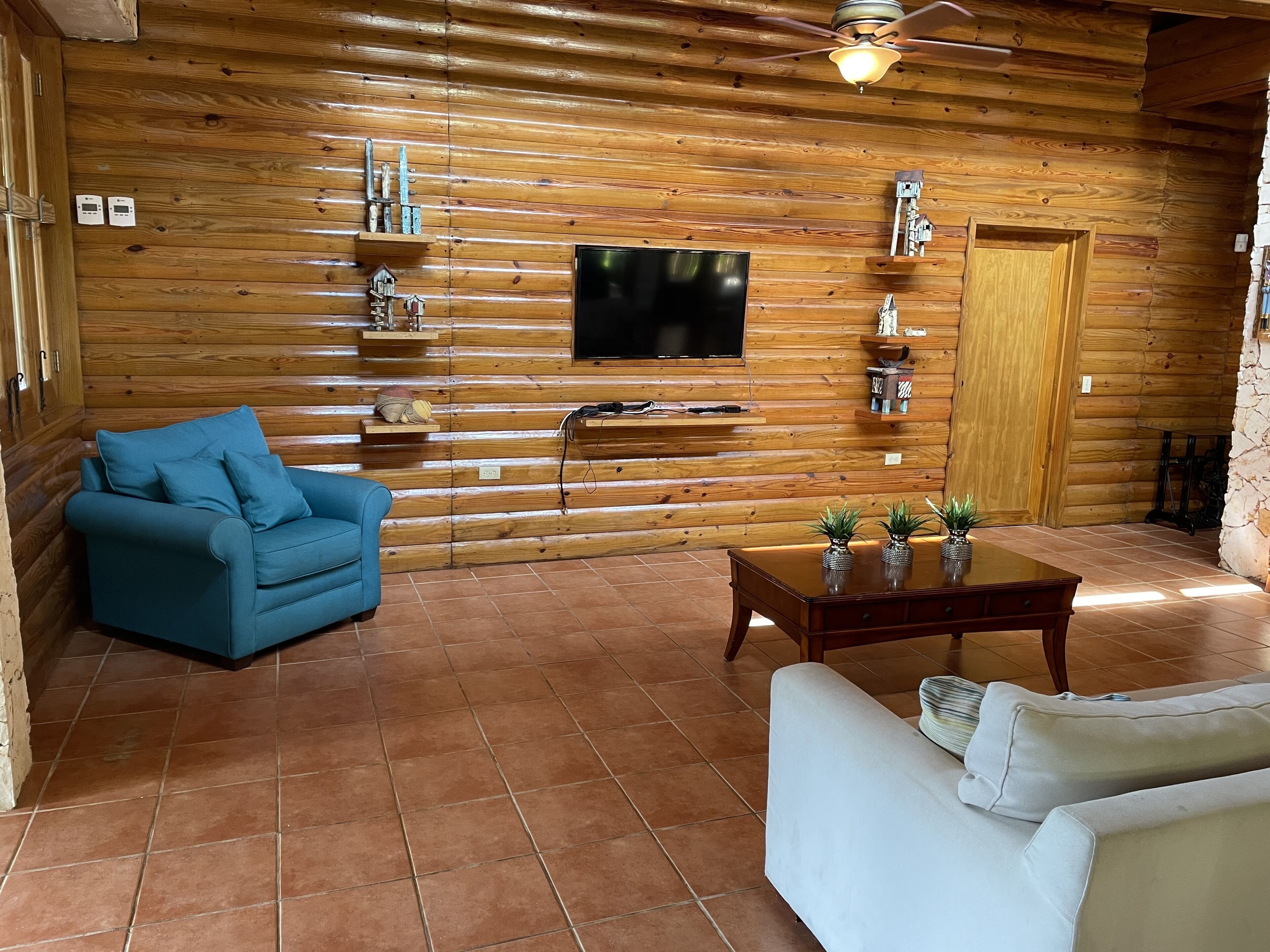 A cozy living room with a blue sofa, a white sofa, a wooden TV stand, and a wooden wall with shelves.