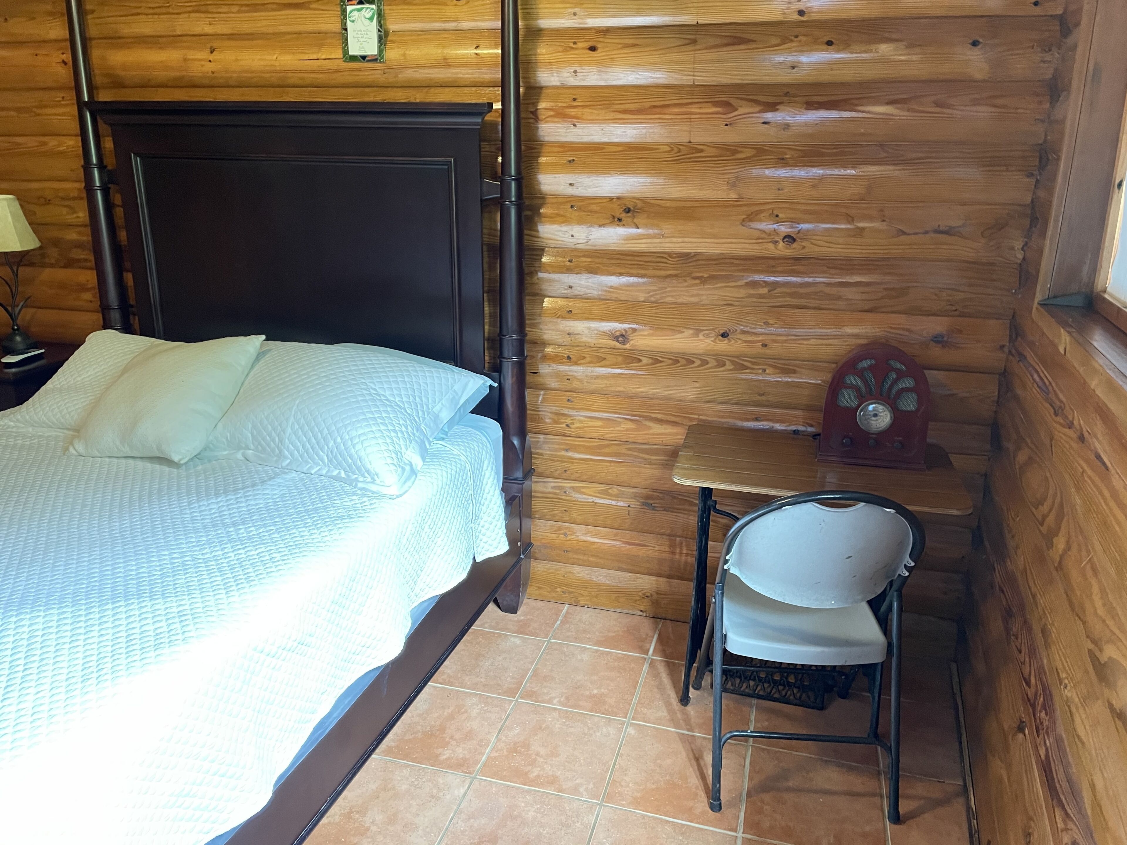 A wooden cabin room with a bed, a small table, and a chair.