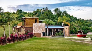 A modern log cabin with a stone foundation, a wooden upper structure, and a covered outdoor area. - Hacienda Elena Paraiso Tropical (Canóvanas)