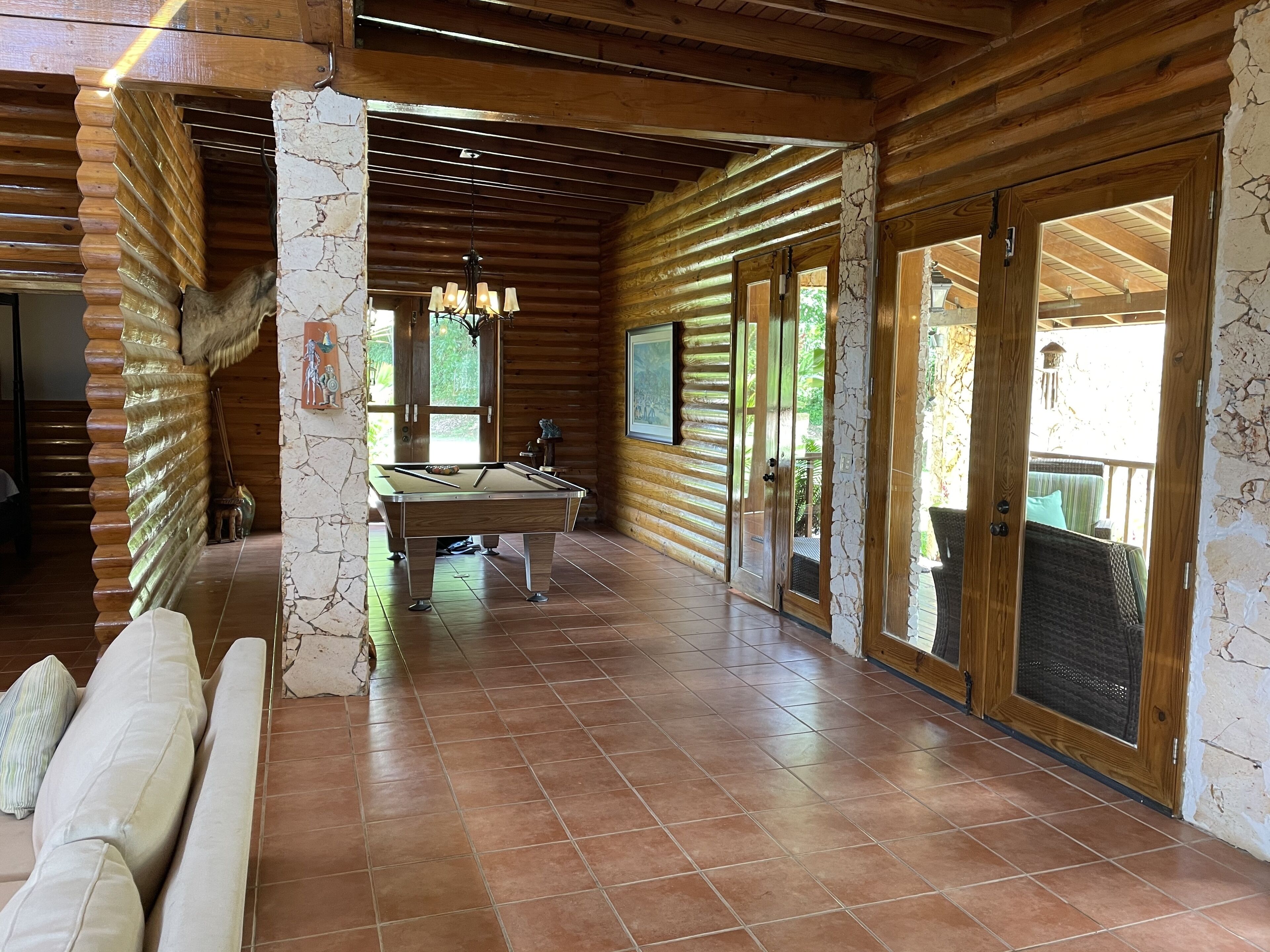 A wooden interior with a pool table, stone pillars, and a balcony with wicker furniture.