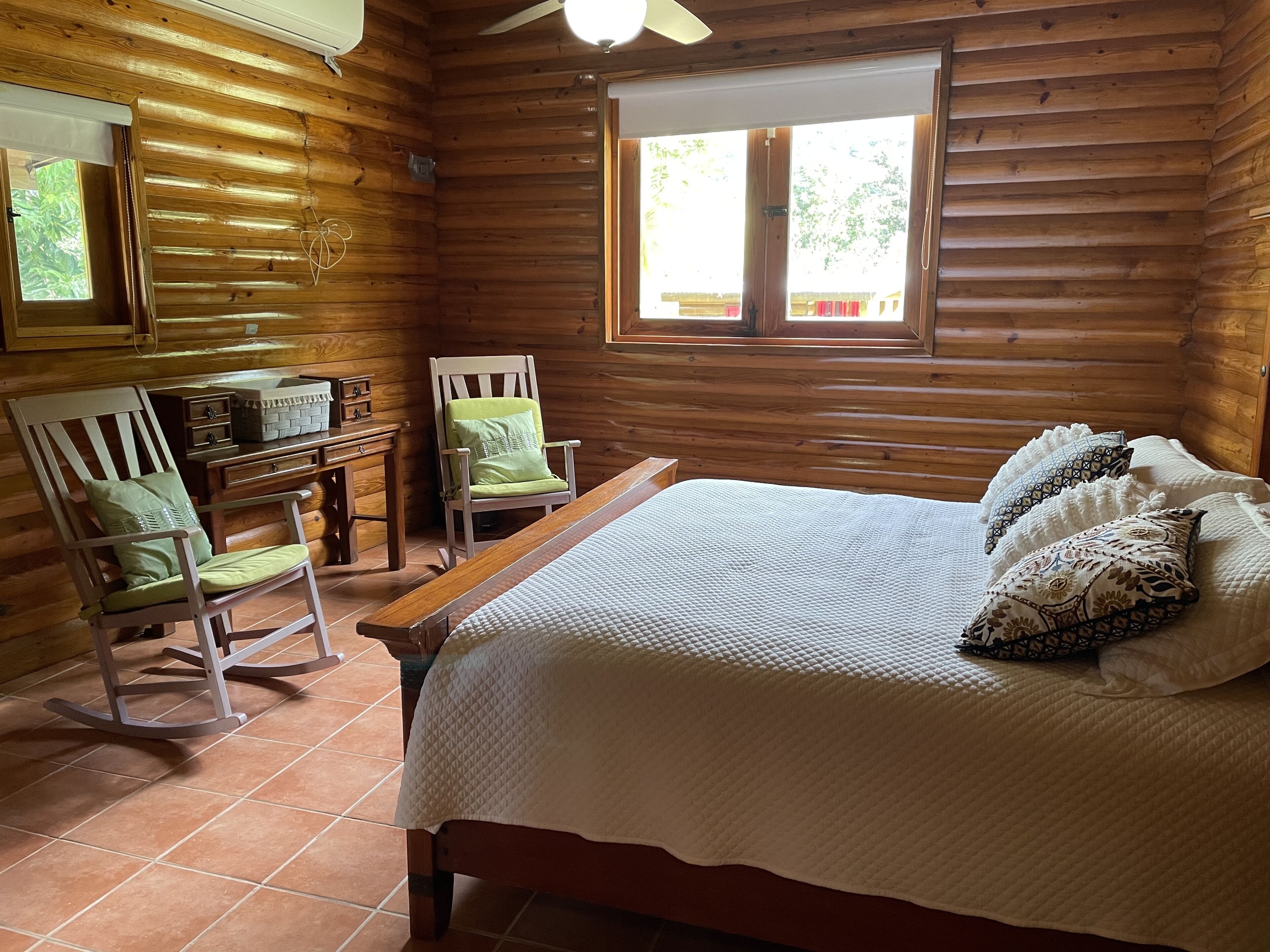 A wooden cabin bedroom with a bed, two chairs, a small table, and a window.