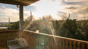 A balcony with a wooden railing, a white chair, and a view of trees and a body of water. - Welcome to Casa Seabrook, your By-The-Sea-Get-Away!! (Seabrook)