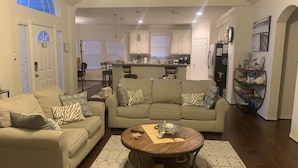 A spacious living room with a beige sofa, a round coffee table, and a dining area in the background. - Welcome to Casa Seabrook, your By-The-Sea-Get-Away!! (Seabrook)
