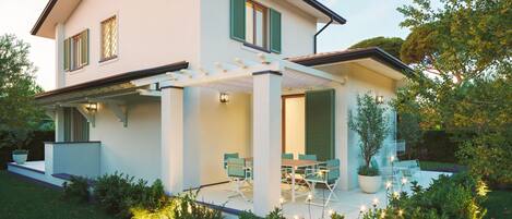 A modern two-story house with a covered patio, outdoor seating, and a well-maintained garden.