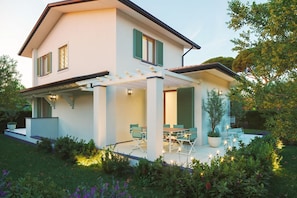 Ein modernes, zweistöckiges Haus mit überdachter Terrasse, Sitzgelegenheiten im Freien und einem gepflegten Garten.