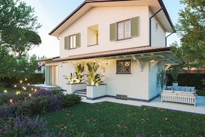 A two-story house with a balcony, a garden with flowers, and a white fence.