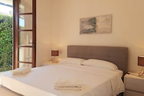 Ein Schlafzimmer mit einem großen Bett, zwei Nachttischen, einem Fenster mit Blick auf Grünflächen und einem Bild an der Wand.