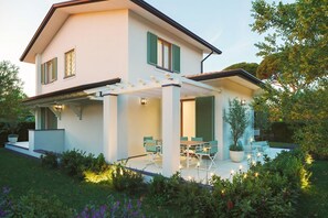 Ein modernes, zweistöckiges Haus mit überdachter Terrasse, Sitzgelegenheiten im Freien und einem gepflegten Garten.