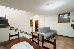 A dining area with a table and chairs, a grey sofa, a staircase, and a wooden cabinet.