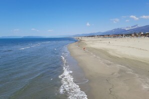 Ein Strand mit blauem Himmel, ruhiger See und Bergen in der Ferne.