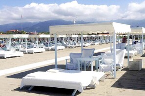 Ein Strandhotel mit weiß beschatteten Sitzbereichen, Liegestühlen und einem Pool.