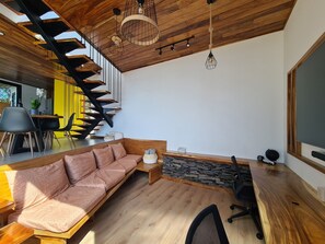 A modern interior with a wooden staircase, a sofa, a desk, and a large window.