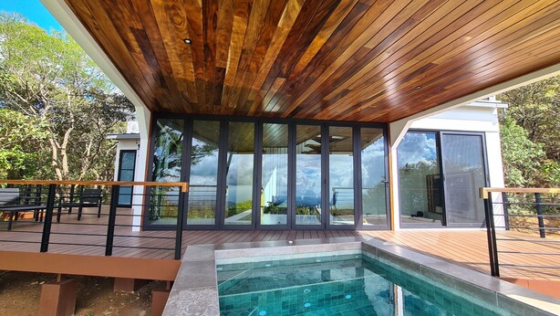 Un espace piscine extérieur moderne, doté d’un plafond en bois, de portes vitrées et offrant une vue dégagée sur le paysage environnant.