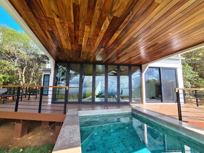 A modern outdoor pool area with a wooden ceiling, glass doors, and a clear view of the surrounding landscape. - A heated pool and breathtaking sunsets. (Monteverde)