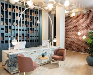 A modern library with bookshelves, a desk with a computer, two chairs, and a brick wall. - Ecole St Pierre Hotel (Istanbul)