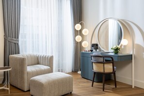 A modern room with a sofa, ottoman, and a vanity with a mirror and lights.