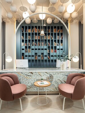 A modern reception area with a large bookshelf, two pink chairs, a laptop, and a decorative table. - Ecole St Pierre Hotel (Istanbul)