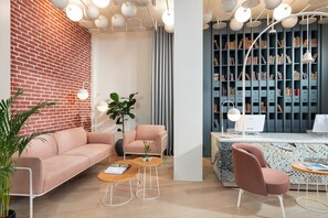 A modern interior with a brick wall, a pink sofa, a wooden coffee table, a desk with a computer, and a bookshelf. - Ecole St Pierre Hotel (Istanbul)