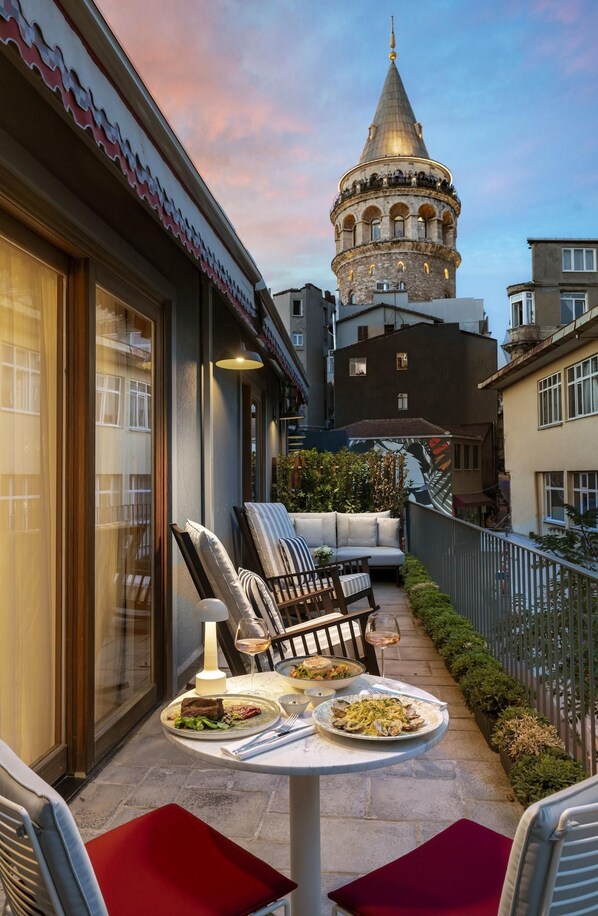 A terrace with outdoor seating, a dining table with plates of food, and a view of a historic tower in the background. - Ecole St Pierre Hotel (Istanbul)