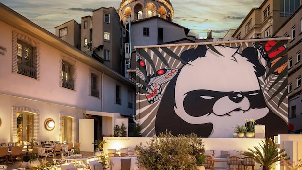 An outdoor dining area with tables and chairs, a large mural of a panda, and a building with a pointed roof in the background. - Ecole St Pierre Hotel (Istanbul)