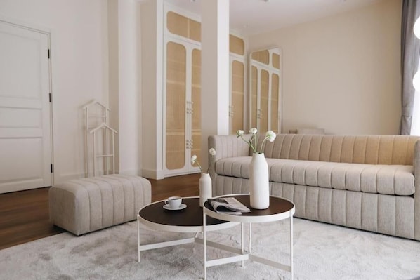 A modern living room with a beige sofa, a round coffee table, and a white ottoman. There are two white vases with flowers on the table. - Ecole St Pierre Hotel (Istanbul)
