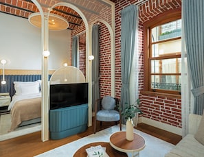 Een moderne slaapkamer met een bakstenen muur, een groot raam, een bed, een televisie en een zithoek met een stoel en een kleine tafel.