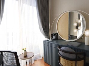 A hotel room with a large round mirror, a small round table with a vase, a dark-colored dresser, and a chair with a woven seat. - Ecole St Pierre Hotel (Istanbul)