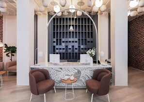 A reception desk with two computer monitors, a vase with flowers, and a patterned wall.