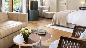 A hotel room with a sofa, a bed, a TV, a small table with a book and flowers, and a chair. - Ecole St Pierre Hotel (Istanbul)