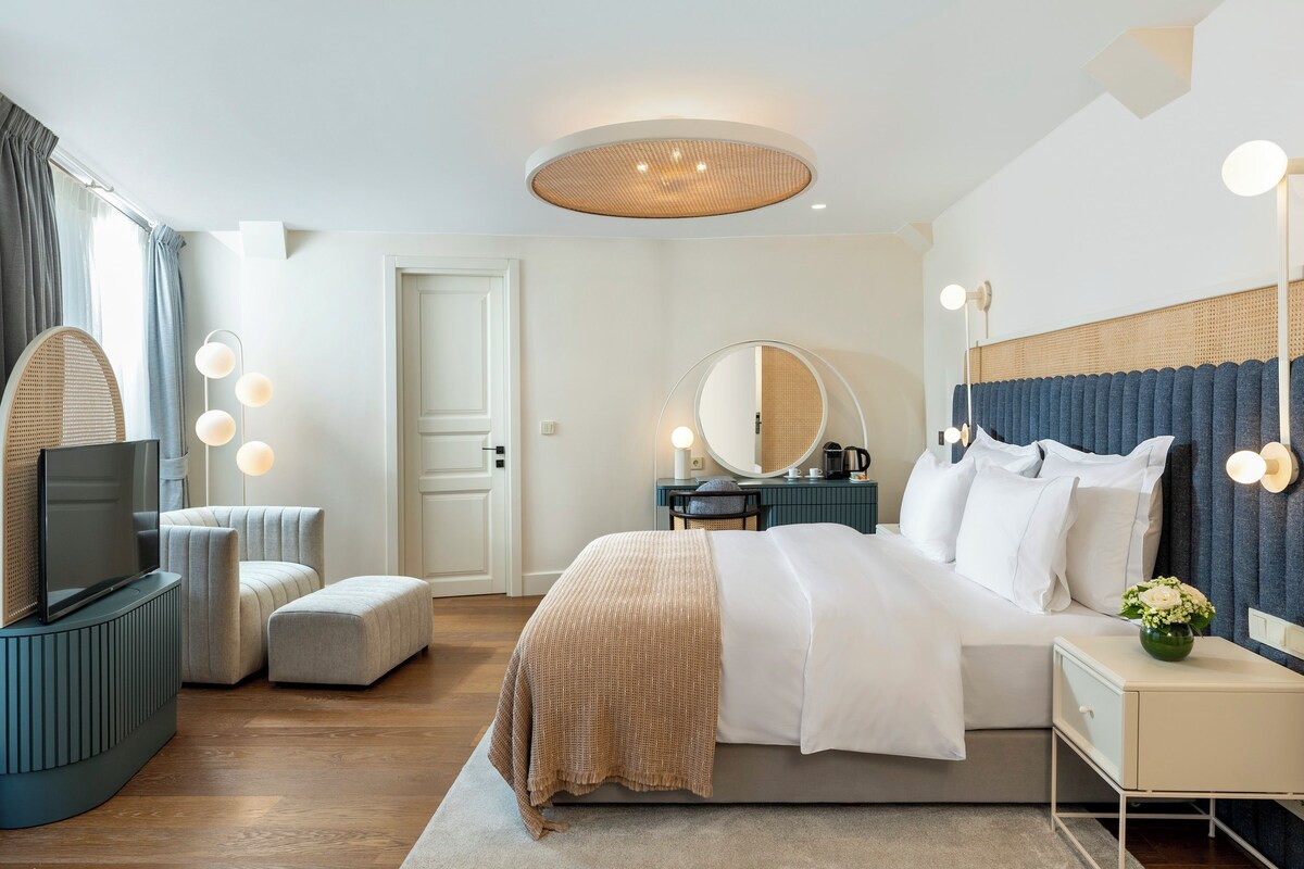 Une chambre d’hôtel moderne équipée d’un lit, d’une table de chevet, d’une télévision et d’un grand miroir.
